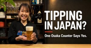 Mizuki-chan smiling and handing a beer across the 6-seat counter at Kaiebi in Shinsaibashi, Osaka