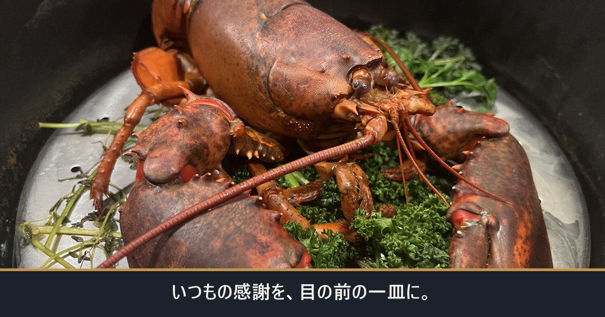 ストウブ鍋の中の活オマール海老と「いつもの感謝を、目の前の一皿に。」の文字