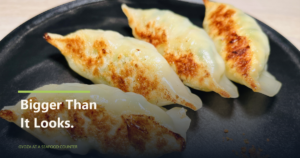 Four pan-seared gyoza on a black plate with the text Bigger Than It Looks.