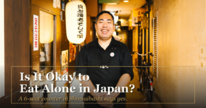 The owner of Kaiebi smiling outside the restaurant entrance under the shop's lantern, with the text Is It Okay to Eat Alone in Japan? A 6-seat counter in Shinsaibashi says yes.