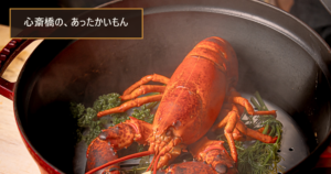 赤い鍋で蒸し上がった活オマール海老とハーブ、立ちのぼる湯気。「心斎橋の、あったかいもん」の文字