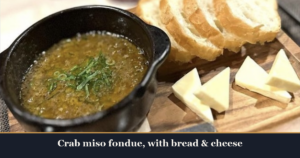 Crab miso fondue in a black pot with sliced bread and cheese on a wooden board at Kaiebi, a 6-seat seafood counter in Shinsaibashi, Osaka