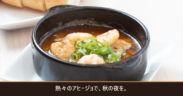 黒い小鍋の海老のアヒージョとバゲット、「熱々のアヒージョで、秋の夜を。」の文字