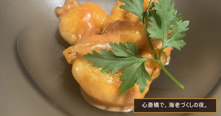 深皿に盛られた、オレンジ色のソースをまとった海老の一皿とイタリアンパセリ。「心斎橋で、海老づくしの夜。」の文字